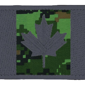 May include: A gray and green camouflage fabric patch with a gray maple leaf in the center. The patch has a gray border.