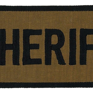 May include: A brown fabric patch with a black border and the word "SHERIFF" embroidered in black.