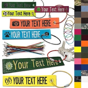 May include: A collection of colorful fabric keychains with the text "Your Text Here" in white. Each keychain has a different icon, including a paw print, camera, soccer ball, and flower. The keychains are attached to metal rings and cables.