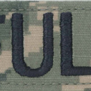 May include: A black and white Air Force patch with the name "FULLER" embroidered in black on a camouflage background.
