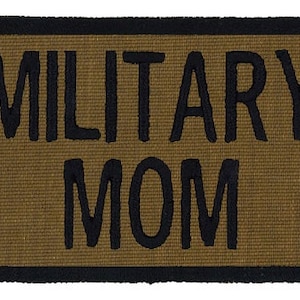 May include: A brown doormat with black trim and the text "MILITARY MOM" in black.