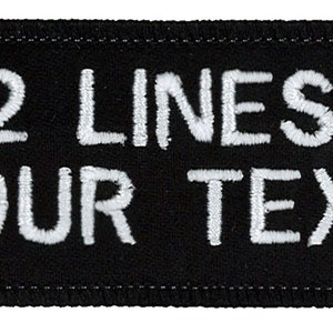 May include: A black rectangular patch with rounded corners. The patch features white embroidered text that reads "2 LINES" above "YOUR TEXT". The patch has a stitched border.