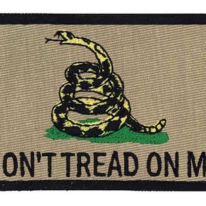 May include: Embroidered patch featuring a coiled rattlesnake in yellow and black on a green patch, set against a tan background. The phrase "DON'T TREAD ON ME" is displayed in black block letters below the snake. The patch has a black border.
