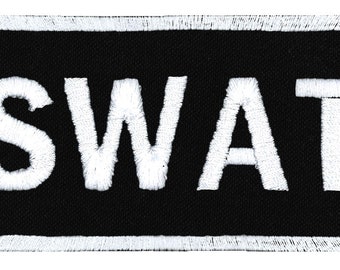 Op de afbeelding: Zwarte rechthoekige patch met witte geborduurde tekst "SWAT".
