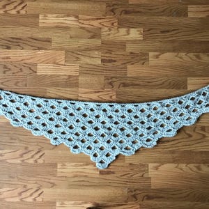 Peut inclure: Une &eacute;charpe en crochet gris clair avec un motif en losange et des glands frang&eacute;s &agrave; chaque extr&eacute;mit&eacute;.
