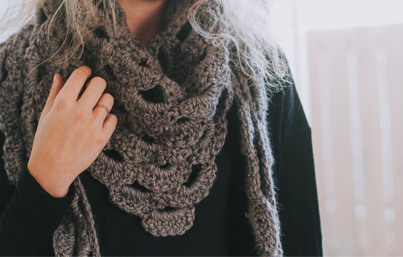 Peut inclure: Gros plan d'une personne portant une &eacute;charpe en crochet marron avec un motif en dentelle. L'&eacute;charpe est drap&eacute; autour du cou et des &eacute;paules de la personne.