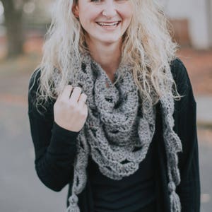Peut inclure: Une femme portant un cardigan noir et une &eacute;charpe en crochet gris avec des glands. L'&eacute;charpe a un motif en dentelle.