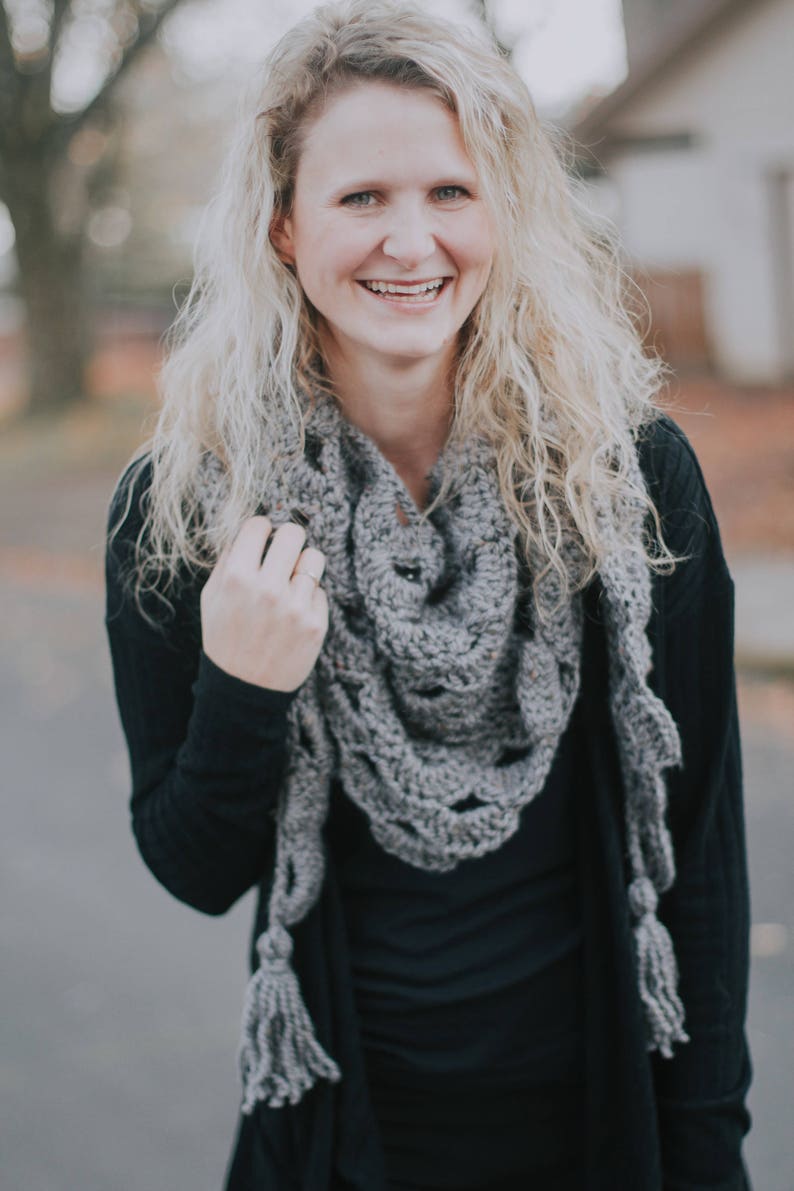 Peut inclure: Une femme portant un cardigan noir et une &eacute;charpe en crochet gris avec des glands. L'&eacute;charpe a un motif en dentelle.