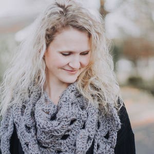 Peut inclure: Une femme aux longs cheveux blonds portant un ch&acirc;le en crochet gris sur un haut noir.