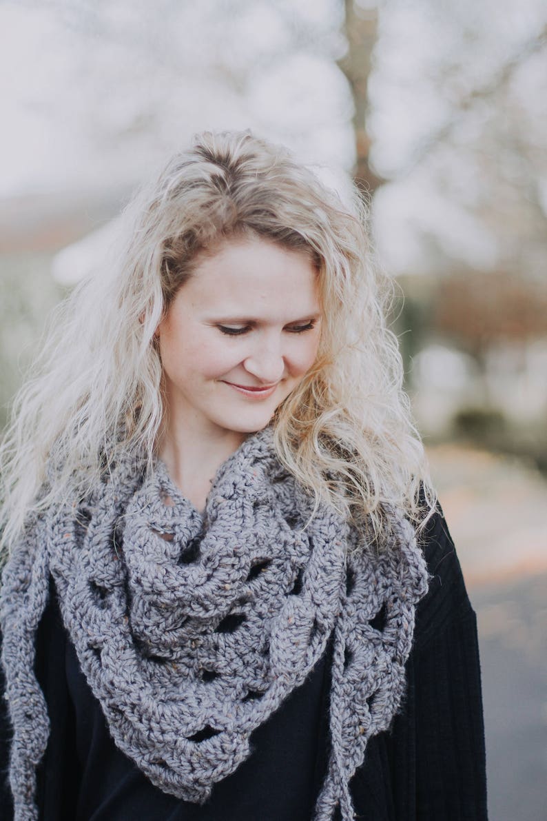 Peut inclure: Une femme aux longs cheveux blonds portant un ch&acirc;le en crochet gris sur un haut noir.