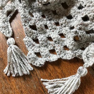 Peut inclure: Un ch&acirc;le en crochet blanc avec un motif mouchet&eacute; et des glands frang&eacute;s.