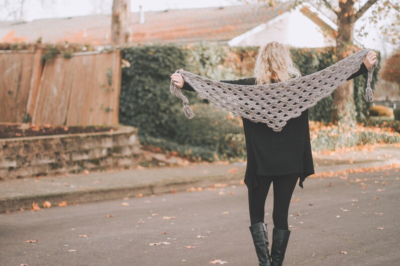 Peut inclure: Une femme portant une &eacute;charpe en crochet grise avec un bord festonn&eacute;. Elle se tient devant une cl&ocirc;ture en bois et de la v&eacute;g&eacute;tation verte.