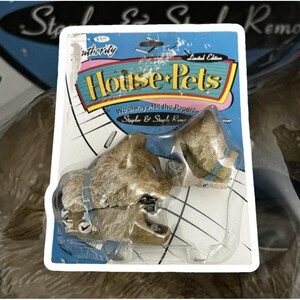 May include: A stapler and staple remover set in a clear plastic package. The packaging features the text "House Pets" and "We always Hit the Paper!" in a colourful design. The stapler and remover are brown and tan.