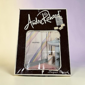 May include: A rectangular Andre Richard product box featuring a cutout window displaying a Calypso shower curtain with diagonal pastel stripes. The packaging includes a white logo, a bathroom scene illustration, and several small adhesive price tags.