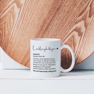May include: White ceramic mug with a black and red design. The mug features the text "Lieblingskollegin" and a definition of the word "Sarah" in German.