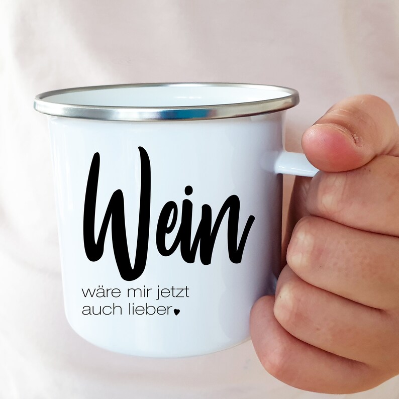 Puede incluir: Taza de esmalte blanco con una inscripci&oacute;n negra que dice "Wein w&auml;re mir jetzt auch lieber" con un peque&ntilde;o coraz&oacute;n negro.