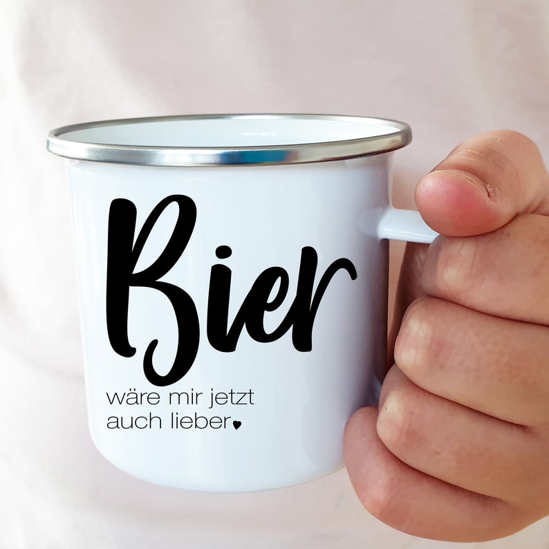 Puede incluir: Taza de esmalte blanco con la palabra "Bier" en cursiva negra y el texto "w&auml;re mir jetzt auch lieber." La taza tiene un borde y un asa plateados.