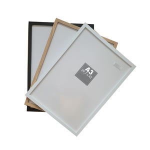 May include: Three picture frames in black, natural wood, and white. The frames are stacked on top of each other. The white frame is on top and has the size A3 (29.7 x 42 cm) printed on it.