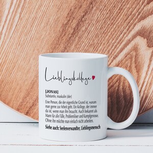 May include: White ceramic mug with a black and red heart design. The mug has a black text that reads "Lieblingskollege [JONAS] Substantiv, maskulin (der) Eine Person, die der eigentliche Grund ist, warum man gerne zur Arbeit geht. Ein Kollege, der immer da ist, wenn man ihn braucht. Auch bekannt als Mann f&uuml;r alle F&auml;lle, Probleml&ouml;ser und Kampfgenosse. Ohne ihn m&ouml;chte man einfach nicht arbeiten. Siehe auch: Seelenverwandter, Lieblingsmensch"