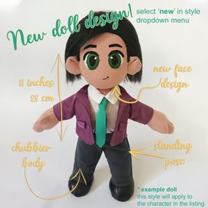 May include: A plush doll with a new face design, standing pose, and chubbier body. The doll is 11 inches (28 cm) tall and wears a purple jacket, green tie, and gray pants. The text says "New doll design!"