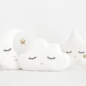 Può includere: Tre cuscini di peluche bianchi a forma di mezzaluna, nuvola e stella. Ogni cuscino ha un viso ricamato nero con gli occhi chiusi. Il cuscino a forma di stella ha un punto di glitter dorato su un lato.