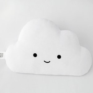 Puede incluir: Almohada blanca en forma de nube con una cara sonriente. La almohada está hecha de tela suave y tiene un diseño simple.