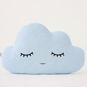 Puede incluir: Una almohada en forma de nube de color azul claro con una cara sonriente y los ojos cerrados. La almohada está hecha de tela suave y es perfecta para la habitación de un niño.