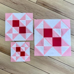 May include: Three square quilt blocks in varying sizes featuring a geometric pattern. Each block is constructed from white, light pink, and solid red fabric pieces arranged in a star-like design with two central red squares placed diagonally.