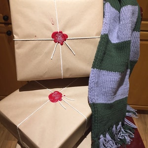 May include: Three wrapped packages tied with string and sealed with red wax. The top package has a white string with a red wax seal. The bottom two packages have a white string with a red wax seal. A green and purple striped scarf with tassels is draped over the packages.