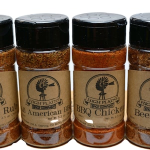 May include: Four glass jars with brown labels and black lids containing different spice rubs. The labels feature a windmill logo and the text "High Plains Spice Company". The spice rubs are labeled "Memphis Rub", "All American BBQ", "BBQ Chicken", and "Beef Rub".