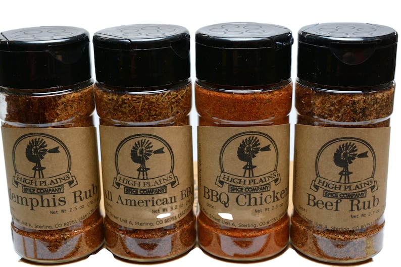 May include: Four glass jars with brown labels and black lids containing different spice rubs. The labels feature a windmill logo and the text "High Plains Spice Company". The spice rubs are labeled "Memphis Rub", "All American BBQ", "BBQ Chicken", and "Beef Rub".