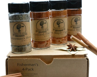 May include: A 4-pack of High Plains Spice Company seasonings in glass jars with brown labels. The flavours are Fisherman's Blend, Grilled Fish, Hot Maple Cajun, and Bristol Bay Spice. The jars are sitting on a brown cardboard box with the text "Fisherman's 4-Pack" printed on the front.