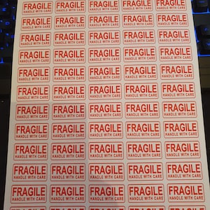 May include: A sheet of red and white "FRAGILE - HANDLE WITH CARE" stickers. Each sticker has a rectangular shape with clear, capitalised text. The stickers are arranged in a grid pattern on a white background.