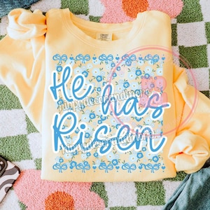 May include: Yellow sweatshirt with a floral pattern and the text "He has Risen" in blue lettering.