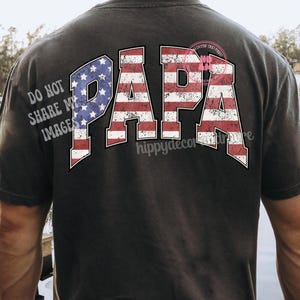 Puede incluir: Una camiseta negra con la palabra "PAPA" impresa en la espalda en letras blancas. Las letras est&aacute;n delineadas en rojo y azul, asemej&aacute;ndose a la bandera espa&ntilde;ola.