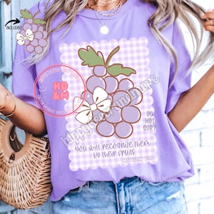 May include: Purple t-shirt with a white and purple gingham pattern and a cartoon image of a bunch of grapes with a bow. The text "you will recognize them by their fruits Matthew 7:16" is printed on the shirt.