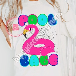 Puede incluir: Camiseta blanca con un gráfico vibrante que presenta un flamenco rosa y las palabras "POOL BABE" en letras de burbujas coloridas. El flamenco tiene un pico dorado y está rodeado de estrellas plateadas.