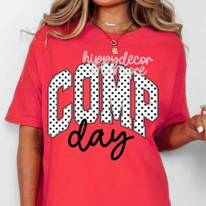 Könnte beinhalten: Ein rotes T-Shirt mit den Worten "COMP day" in fetter, schwarzer Schrift. Das Wort "COMP" ist in weißer Schrift mit schwarzen Punkten gehalten. Der Text "hippydecor" steht über dem Wort "COMP".