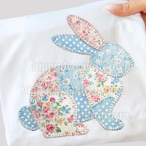 May include: White fabric with a patchwork bunny design. The bunny is made from blue polka dot and floral patterned fabrics with pink and white flowers. The design is stitched onto the fabric.