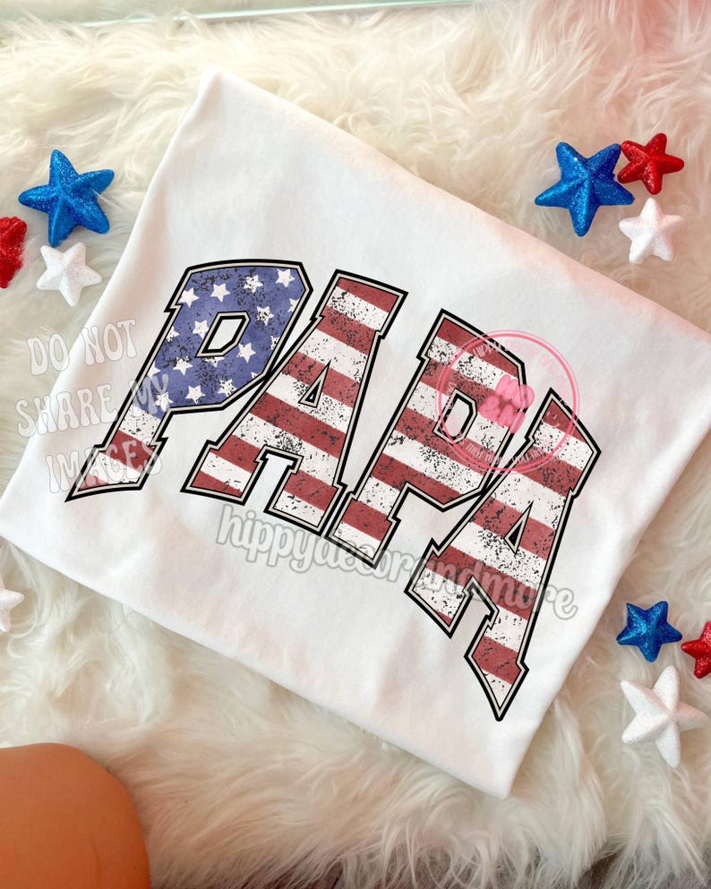 Puede incluir: Camiseta blanca con la palabra "PAPA" en letras de bandera estadounidense roja, blanca y azul desgastadas.