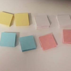 May include: Assortment of colorful sticky notes in yellow, blue, pink, and white. The notes are stacked in piles and arranged in rows on a white surface.