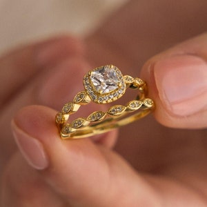 May include: A gold engagement ring set with a large, square-cut diamond surrounded by smaller diamonds. The ring is set on a band with a delicate, scalloped design.