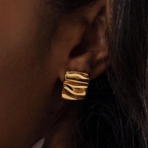May include: Gold-toned, layered, geometric earrings. The earrings are made of a smooth, textured metal and have a slightly curved shape.