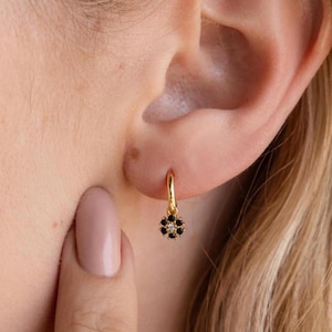 May include: Gold hoop earrings with a small black flower charm featuring tiny clear stones.