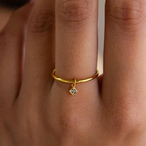 May include: A gold ring with a small, square-shaped, clear gemstone dangling from it.