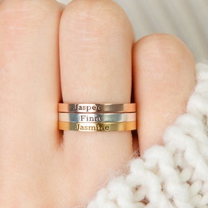May include: Three gold, silver, and rose gold stacking rings with the names "Jasper", "Finn", and "Jasmine" engraved on them.