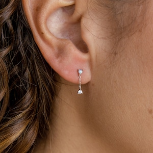 Puede incluir: Un par de delicados pendientes de oro con pequeños detalles de diamantes. Los pendientes tienen una cadena colgante con un pequeño diamante en el extremo.