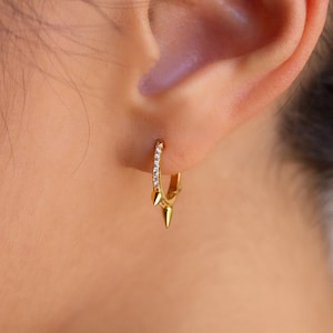 May include: Gold hoop earrings with a row of small clear stones and a pointed spike design.