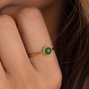 May include: A gold ring with a small, round green gemstone.