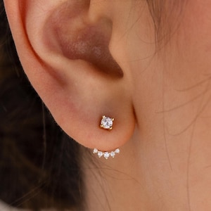 May include: A pair of gold earrings with a single diamond in the center and a row of smaller diamonds along the bottom edge.